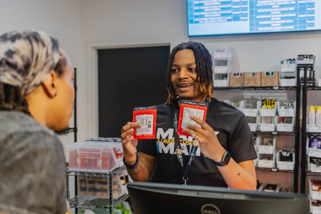 Smiling store employee holding two red packages while assisting a customer at the counter